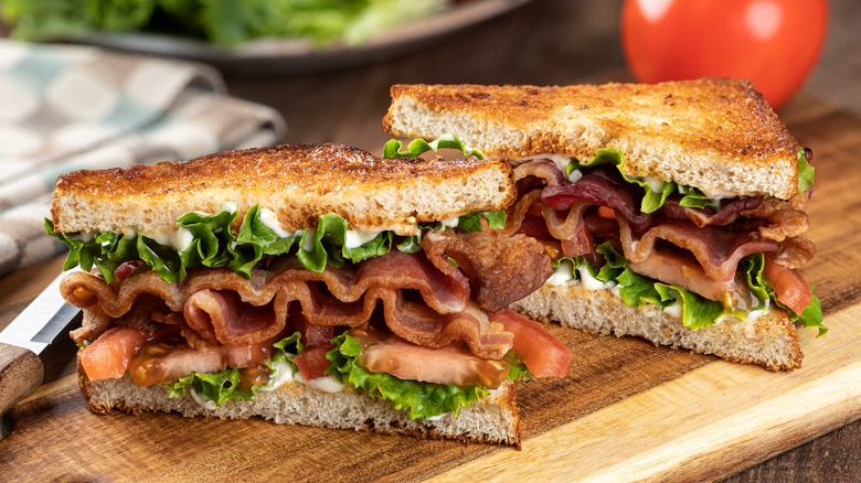 two halves of a BLT sandwich sitting on a wooden surface