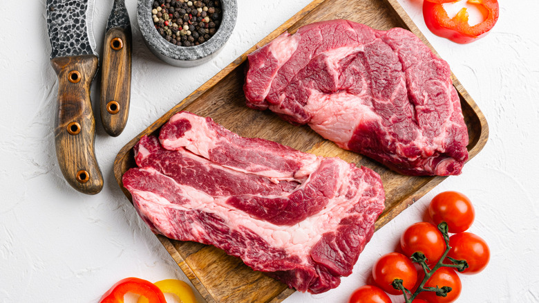 Raw chuck steaks on wooden platter