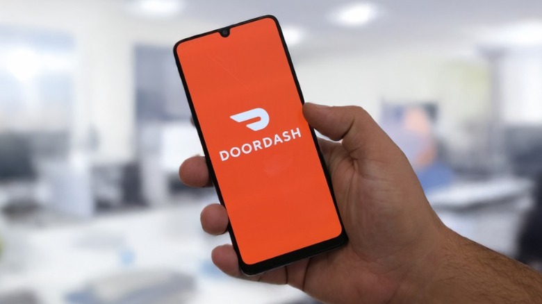 A man holding a smartphone with the DoorDash app logo on the screen.