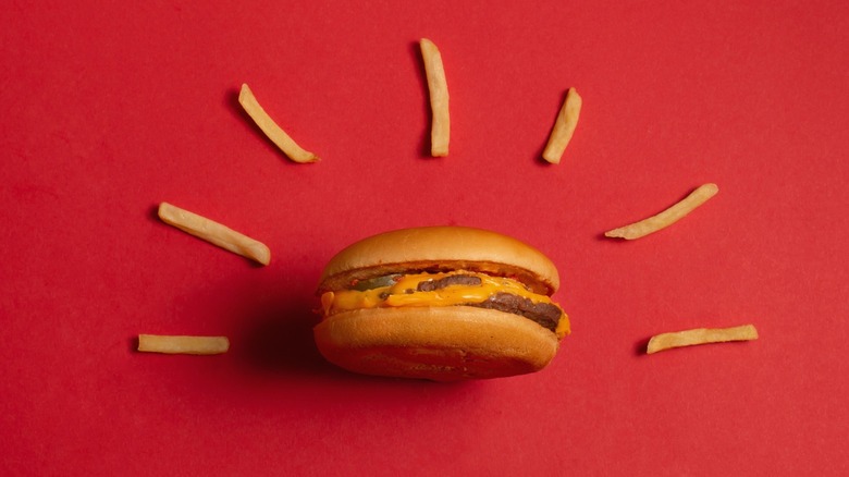 A minimalist depiction of a McDonald's hamburger surrounded by sun ray like fries on a red background