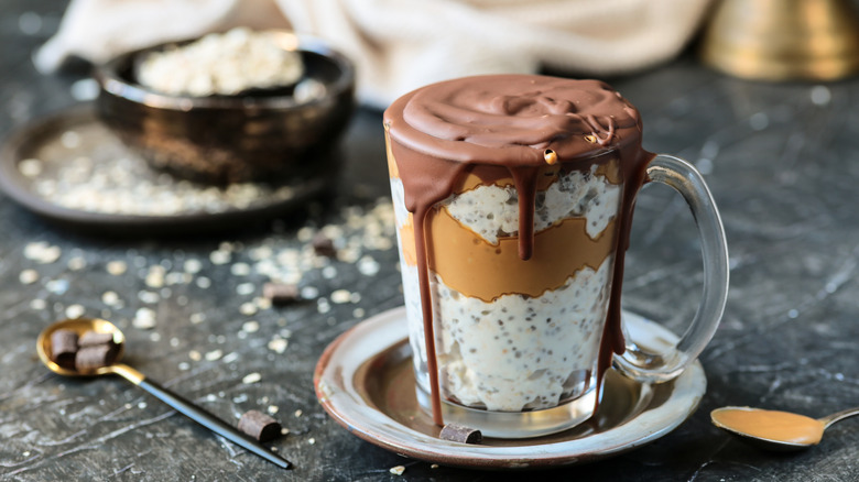 glass of overnight oats with layers of chia seeds and peanut butter, topped with chocolate drizzle