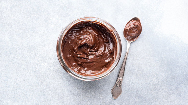 glass jar of thick and creamy chocolate peanut spread over white background