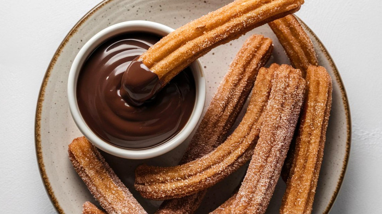 Chocolate dip and churros on a light plate with white background.