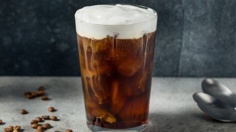 glass of iced coffee topped with a layer of thick, creamy cold foam gently melting into coffee