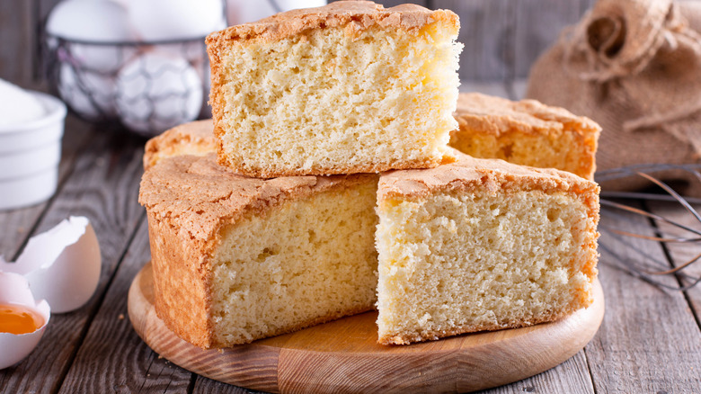 Yellow cake cut into slices and stacked on a wooden disc plate.