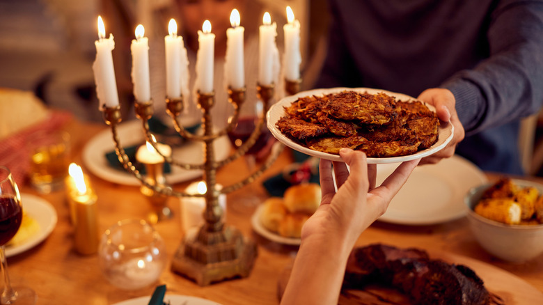 hands holding a plate of latkes in front of a lighted menorah