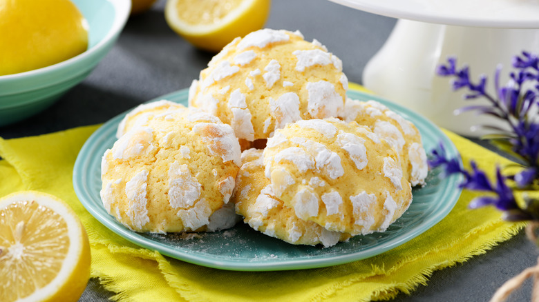 Lemon crinkle cookies on a teal plate accompanied by sliced lemons nearby.