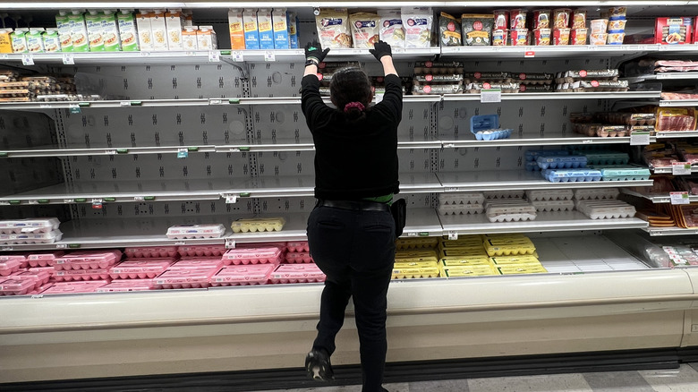 A grocery store employee arranges products in an empty egg section