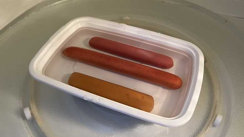 Hot dogs are sitting in water in the microwave.