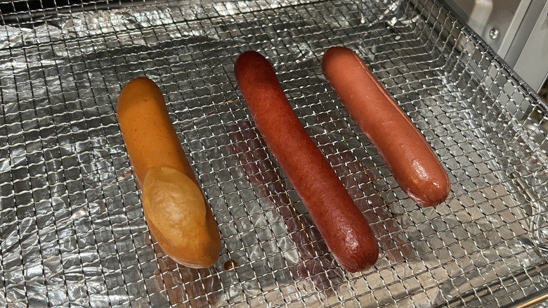 Three hot dogs sit in an air fryer basket.