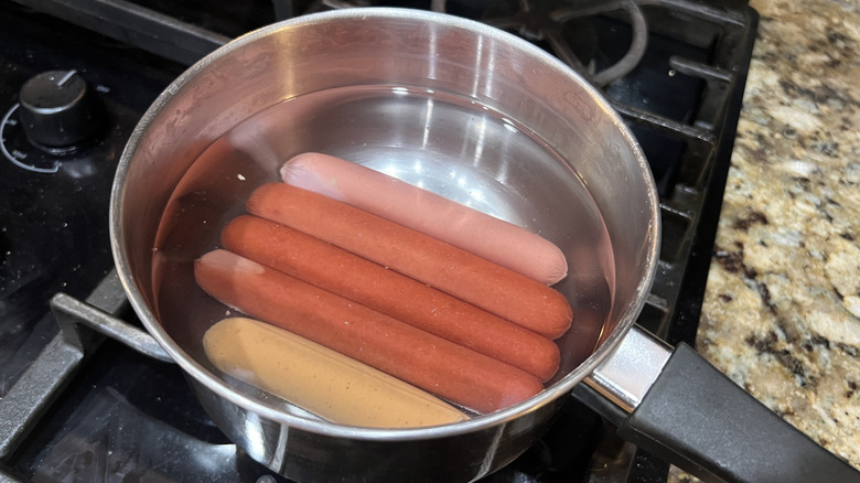 Hot dogs are boiling in water in a pan on the stove.