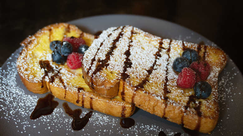 two pieces of french toast garnished with fruit and powdered sugar