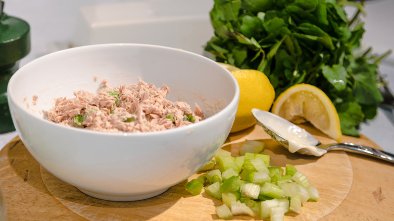 Bowl of tuna salad alongside celery, lemon, and parsley