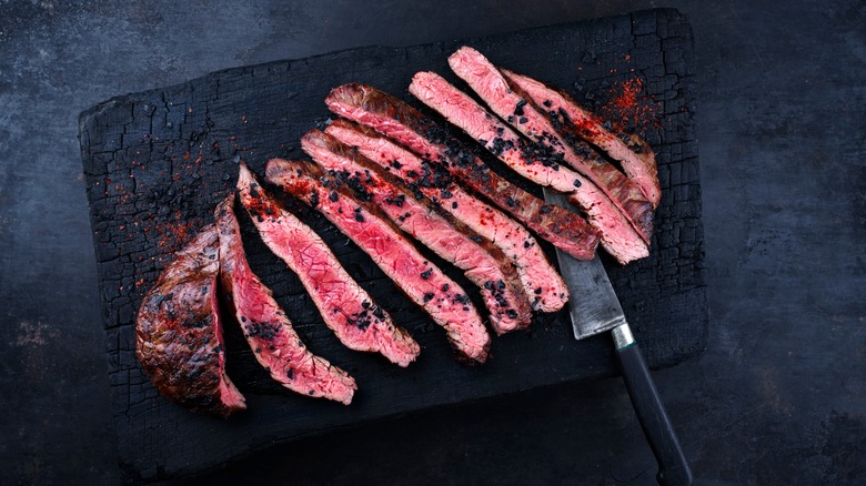 Sliced, grilled flank steak served on a charred-wood cutting board