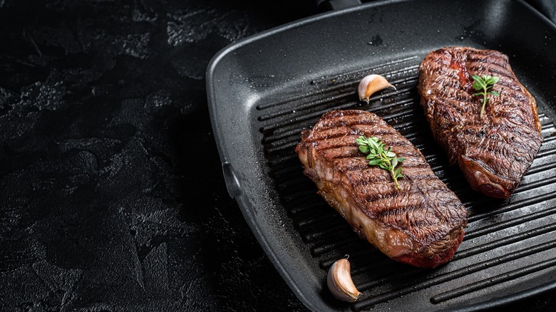 Two flat iron steaks on a grill pan with garlic