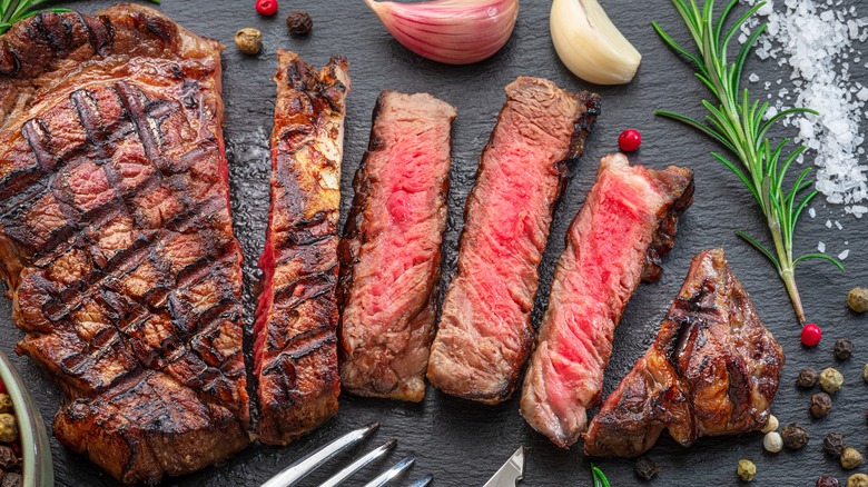 Grilled ribeye on a platter with rosemary, garlic, and peppercorns