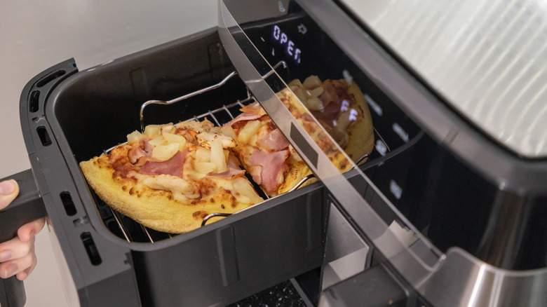 Person pulling air fryer basket out with pizza in it