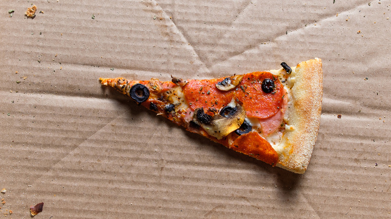 Slice of leftover pizza on cardboard