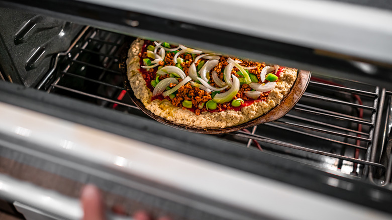 Person opening oven door with pizza inside