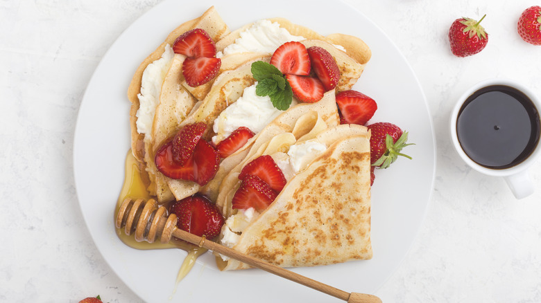 Top view of folded crepes on a plate with ricotta cheese filling, drizzled with honey and cut strawberries on top