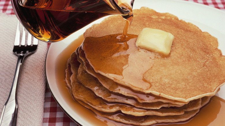 Plate of pancakes with butter pats on top and syrup being poured on top