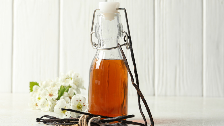 Homemade vanilla extract in a sealed glass bottle with vanilla pods in front of it