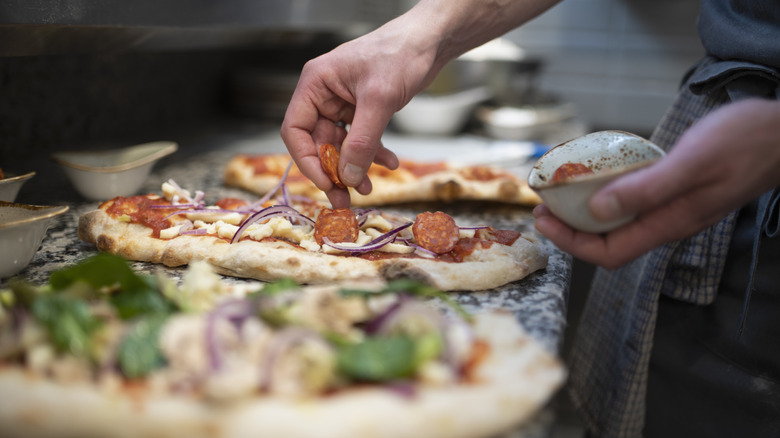 Person adding ingredients to three pizzas