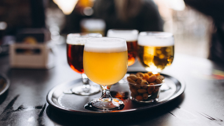 A tray with four glasses of beer and a plastic tub of peanuts