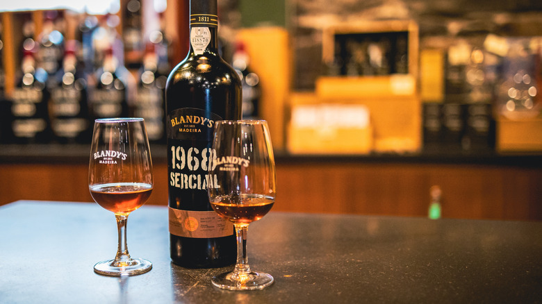 Two glasses of Blandy's Madeira wine next to a corked bottle on a bar counter