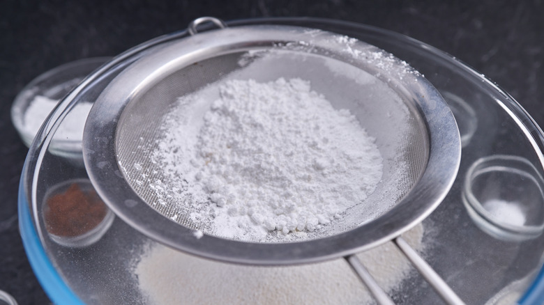 Sifting powdered sugar into a bowl of dry ingredients