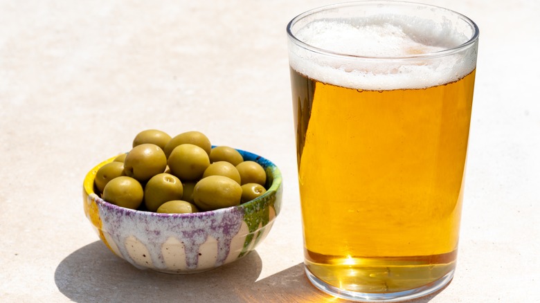 Glass of light beer sitting next to a bowl of green olives