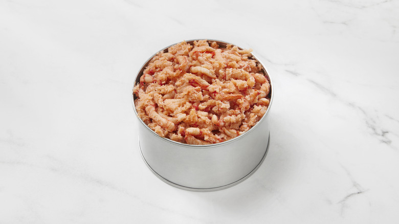 A grey tin filled with pink pieces of crab sits atop a white marble counter