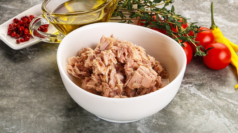 A white bowl of canned tuna foregrounds a cup of oit, some tomatoes and peppers