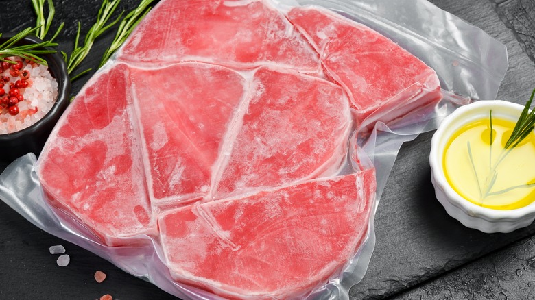 A package of frozen tuna steaks on a counter, a ramekin of oil alongside