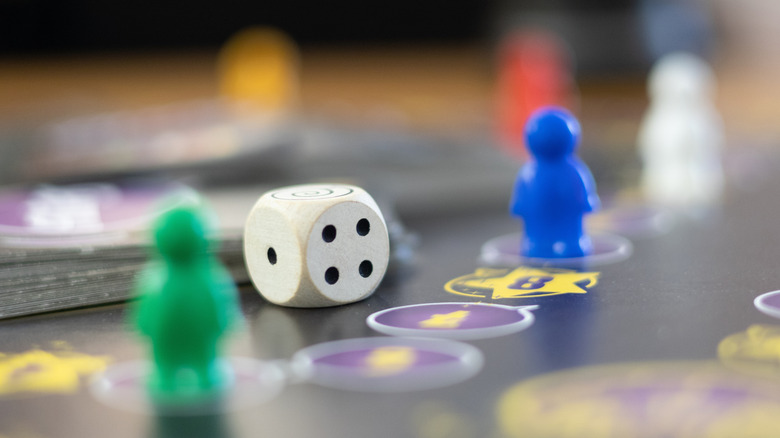 Closeup of a die and two game pawns on a board with cards