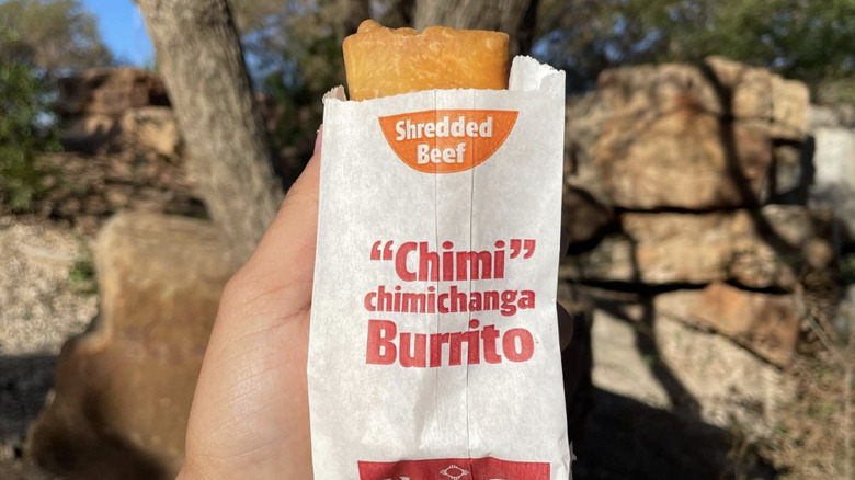 Hand holding an Allsup's chimichanga burrito in front of a tree