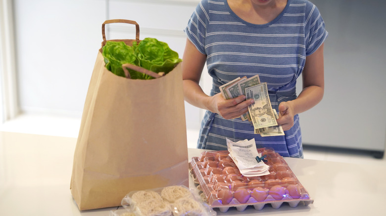 woman counting money with groceries