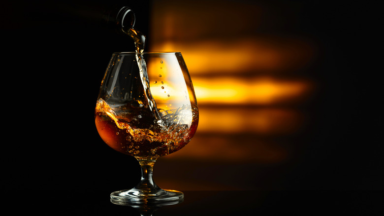 Cognac being poured from botte to snifter on dark background