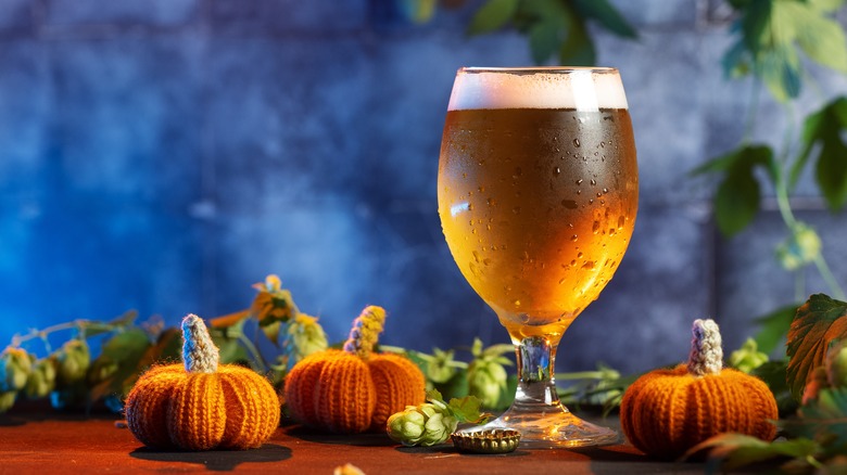 pumpkin beer in a glass surrounded by knitted pumpkin decorations