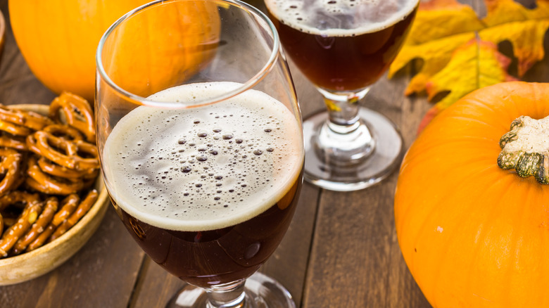 glasses of pumpkin beer with pumpkins, leaves, and a bowl of pretzels