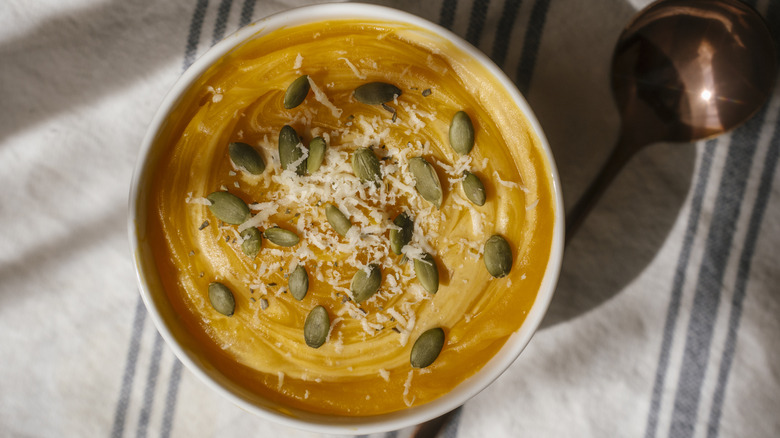 Autumn Squash soup in a white bowl on a striped cloth with a copper spoon.