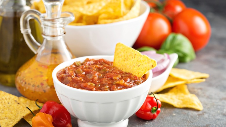 A bowl of red salsa with a corn chip dipped in it.