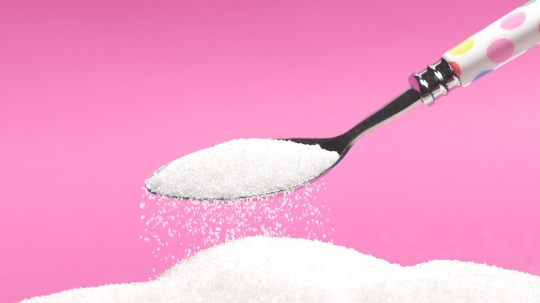 A spoonful of white sugar above a pile of white sugar