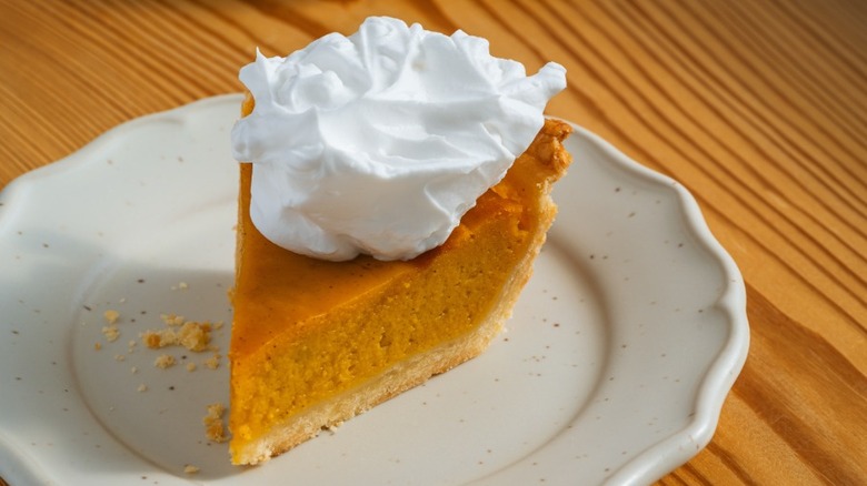 a slice of pumpkin pie on a plate with whipped cream