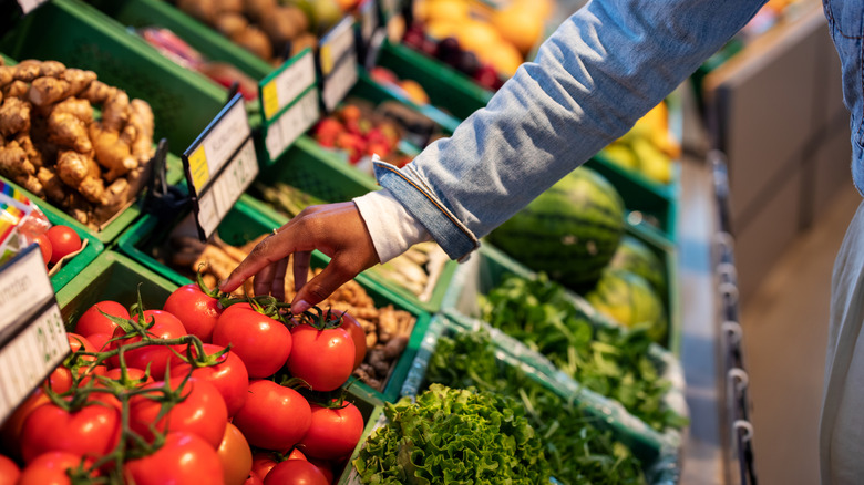 Someone reaching for tomatoes in a produce aisle