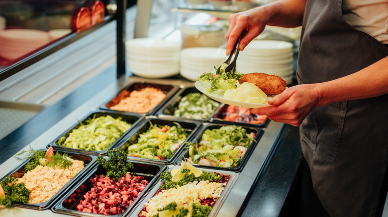 A person putting food on their plate at a salad buffet.