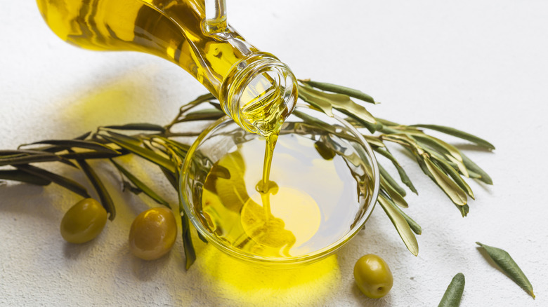 Olive oil being poured from a glass bottle into a small glass bowl