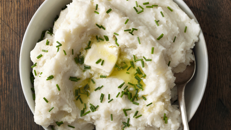 A dish of mashed potatoes topped with chives and butter