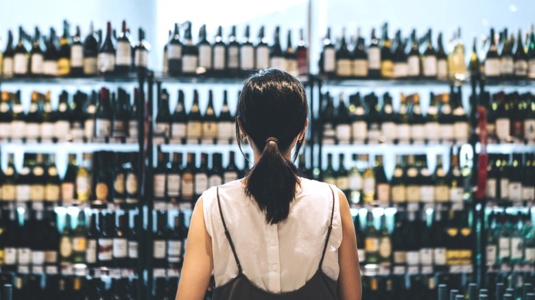 A women stares at several rows of wine in a store.