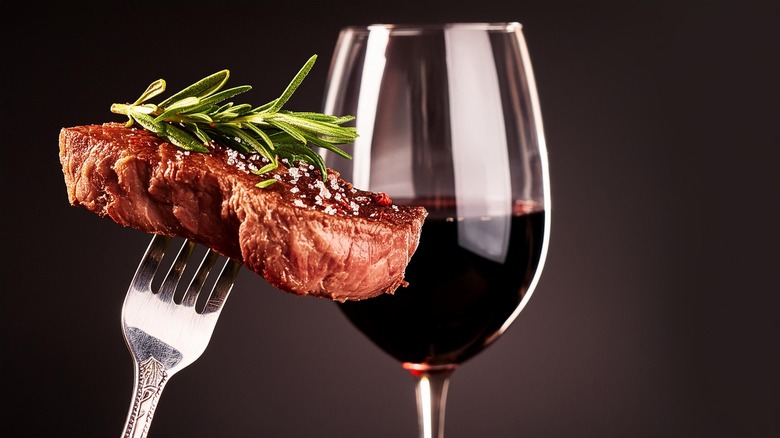 A beautifully sliced steak dinner with utensils, napkin, and a glass of red wine on slate background.